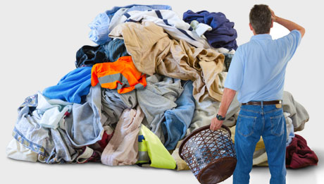 Schluss mit weiterlaufenden Bekleidungskosten in Corona-Zeiten! Mann von hinten zu sehen, steht in grübelnder Haltung mit Wäschekorb vor einem Berg Wäsche