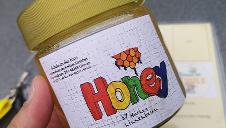 Hand hält Honigglas mit buntem Etikett